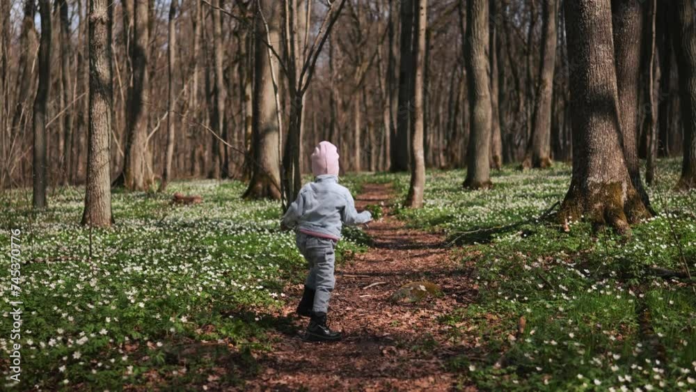 Little girl running away in the forest covered with anemones 