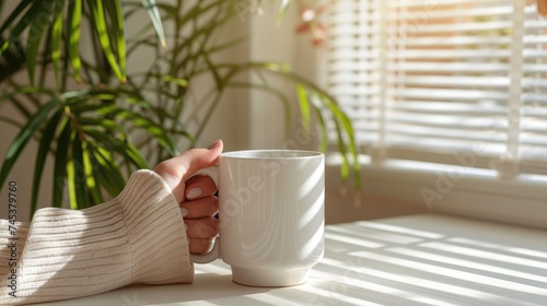 Woman's one hands holds a standard white mug, placed on the table. MOst of the mug is visible.