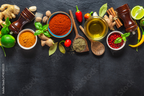 Colorful food cooking ingredients background with various herbs and spices on on a dark stone background top view