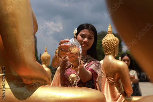 Asia women in Thai traditional dress holding lotus flower and silver Bowl to pray respect and Sprinkle water onto a Buddha image photo