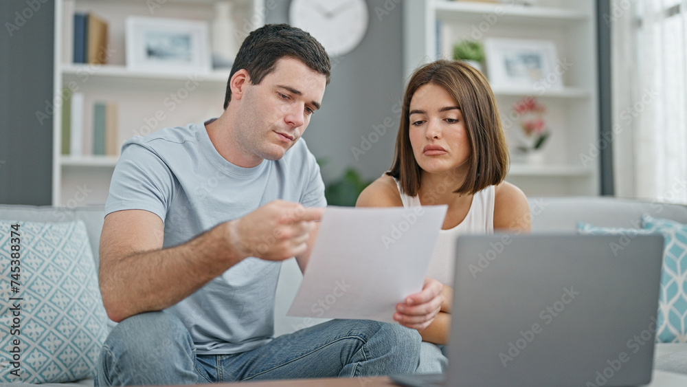 Beautiful couple using laptop reading document sitting on sofa at home Beautiful couple using laptop reading document sitting on sofa at home