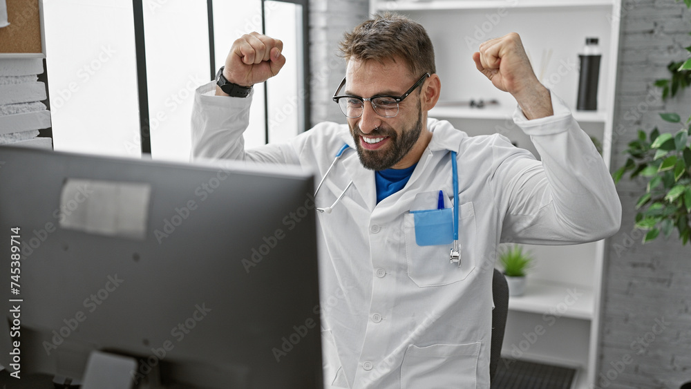 Fototapeta premium Triumphant win! young hispanic male doctor celebrates working diagnosis at the clinic, confident smile behind glasses, bearded and handsome