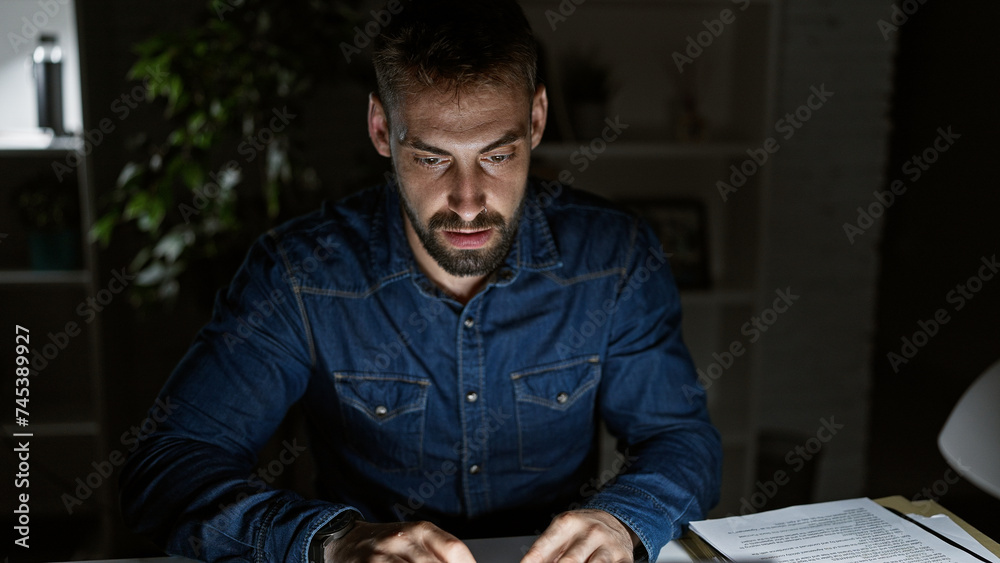 Driven young hispanic man, working long nights at office; focused, serious yet relaxed, this bearded professional navigates business on his laptop. Driven young hispanic man, working long nights at office; focused, serious yet relaxed, this bearded professional navigates business on his laptop.