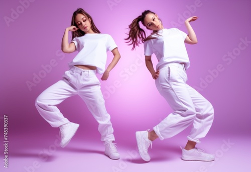 Two girls engaging in a synced dance routine against a pink backdrop.