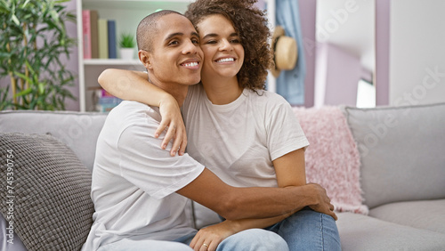 Beautiful couple sitting on sofa, hugging with radiant smiles in their cozy home. a testament of love, an expression of joy and confidence reigns in the room as their casual lifestyle shines through.