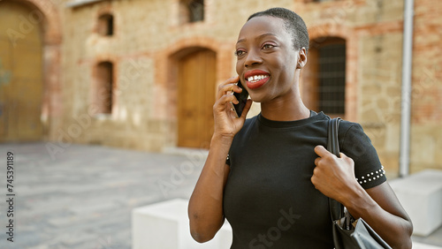 Confident african american woman, radiating positivity, enjoys a sunny city park while cheerfully talking on her smartphone © Krakenimages.com