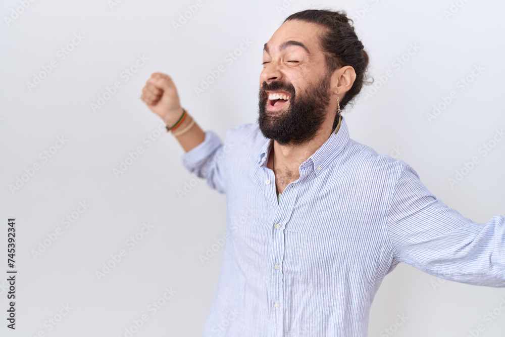 Hispanic man with beard wearing casual shirt dancing happy and cheerful, smiling moving casual and confident listening to music