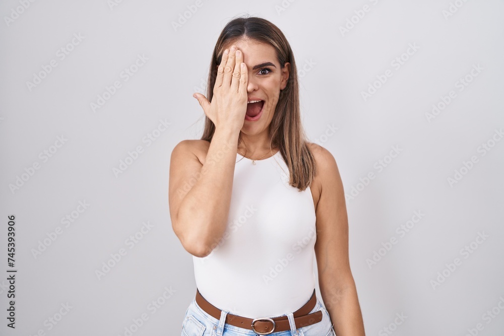 Φωτογραφία Hispanic young woman standing over white background covering one eye with hand, confident smile on face and surprise emotion
