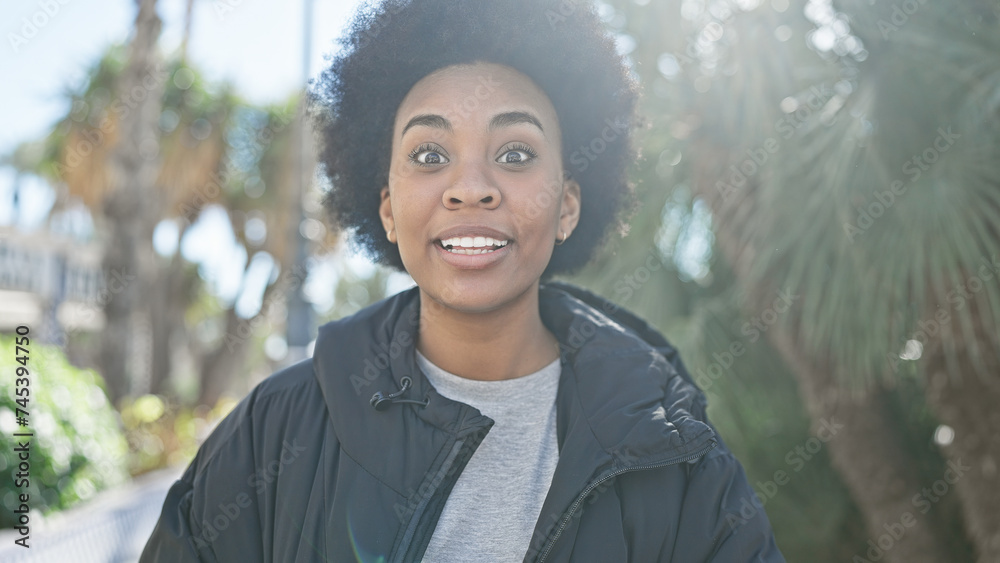 African american woman with curly hair smiling outdoors in a city park surrounded by greenery. African american woman with curly hair smiling outdoors in a city park surrounded by greenery.