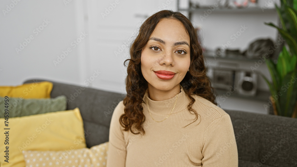 Portrait of a smiling young mixed race woman indoors, comfortably posing at home in a modern living room. Portrait of a smiling young mixed race woman indoors, comfortably posing at home in a modern living room.