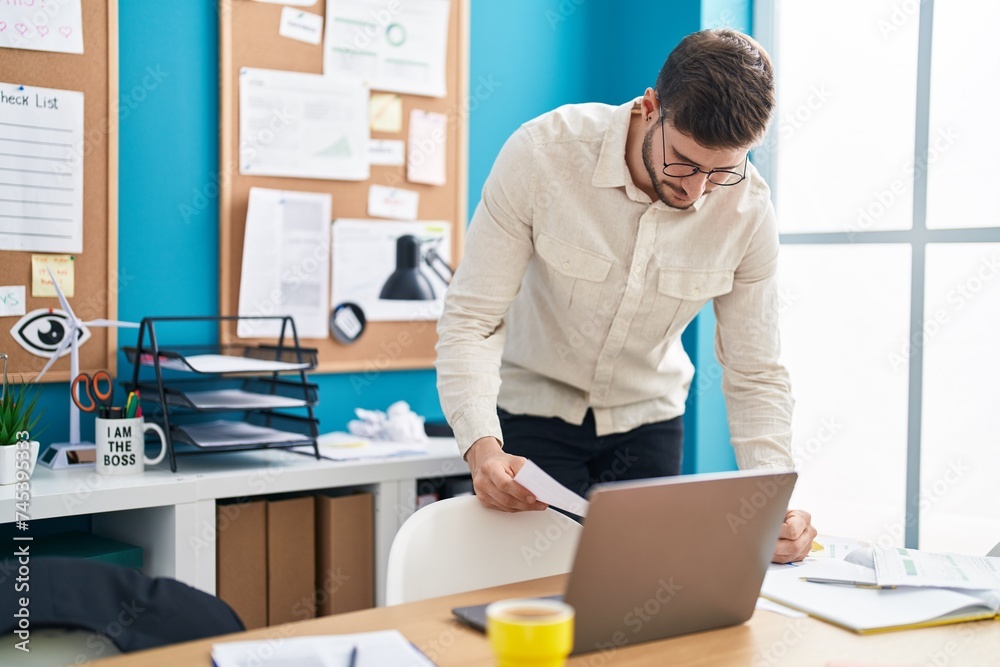 Young caucasian man business worker using laptop writing on document at office Young caucasian man business worker using laptop writing on document at office