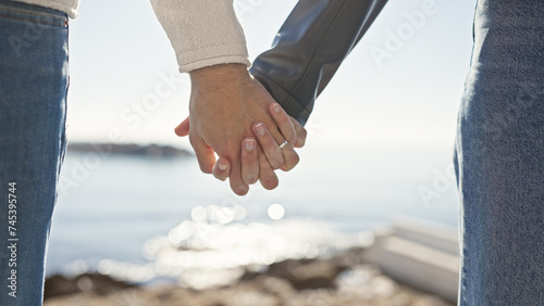 Couple holding hands at the seaside signifies love and connection amidst a beautiful ocean backdrop.