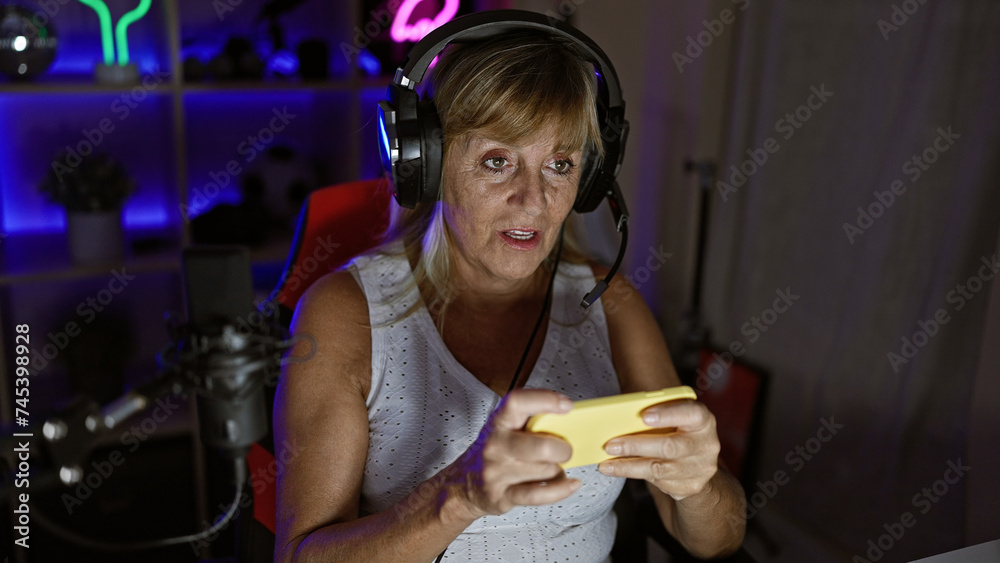 Blonde middle-aged woman streamer dominates mobile game during epic late-night stream in her dark gaming room