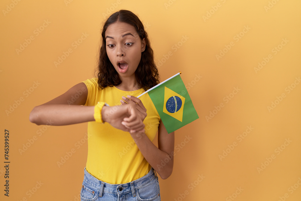 Young hispanic woman holding brazil flag looking at the watch time worried, afraid of getting late Young hispanic woman holding brazil flag looking at the watch time worried, afraid of getting late