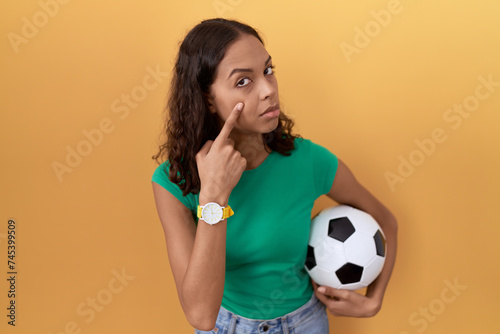 Young hispanic woman holding ball pointing to the eye watching you gesture, suspicious expression © Krakenimages.com