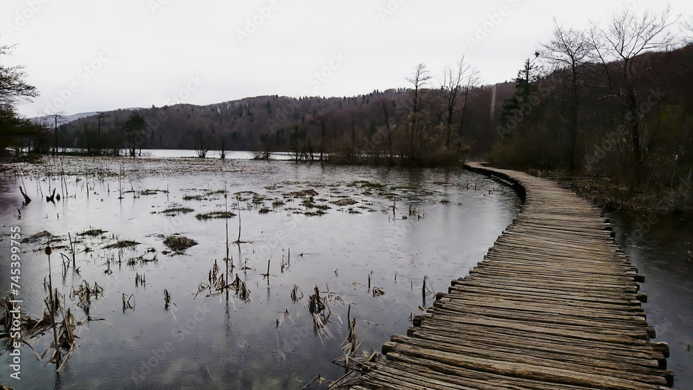 Plitvice Lakes National Park, Croatia - 04.12.2018: An empty wooden bridge crossing a lake leading into a forest on a rainy day Plitvice Lakes National Park, Croatia - 04.12.2018: An empty wooden bridge crossing a lake leading into a forest on a rainy day