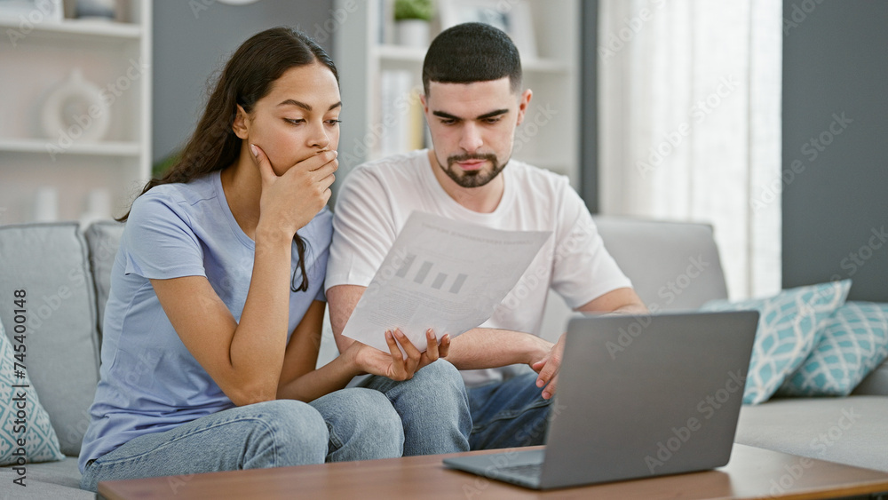 Stressed beautiful couple at home, reading upsetting document on laptop, worrying together in their living room Stressed beautiful couple at home, reading upsetting document on laptop, worrying together in their living room
