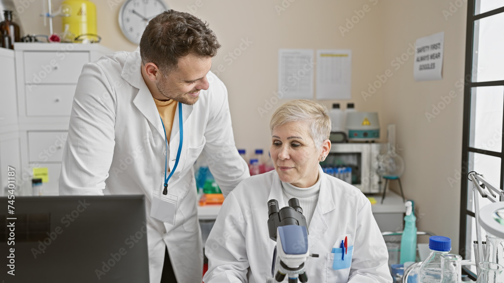Woman and man scientists collaborating in a laboratory filled with equipment, discussing research findings. Woman and man scientists collaborating in a laboratory filled with equipment, discussing research findings.