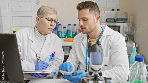 A woman and a man in lab coats work collaboratively in a scientific laboratory  researching with microscope and notes.