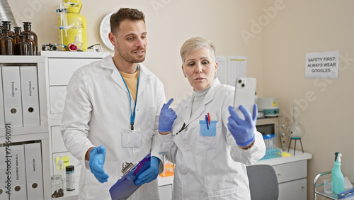 A man and woman  both scientists  are analyzing data on a smartphone together in a laboratory setting.