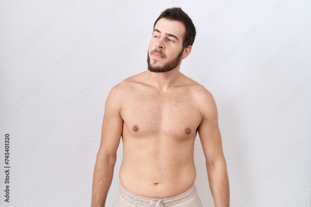 Young hispanic man standing shirtless over white background smiling looking to the side and staring away thinking.
