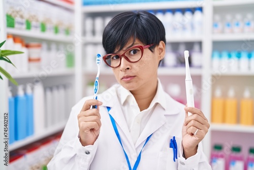 Young asian woman with short hair doing toothbrush comparative at pharmacy skeptic and nervous, frowning upset because of problem. negative person.