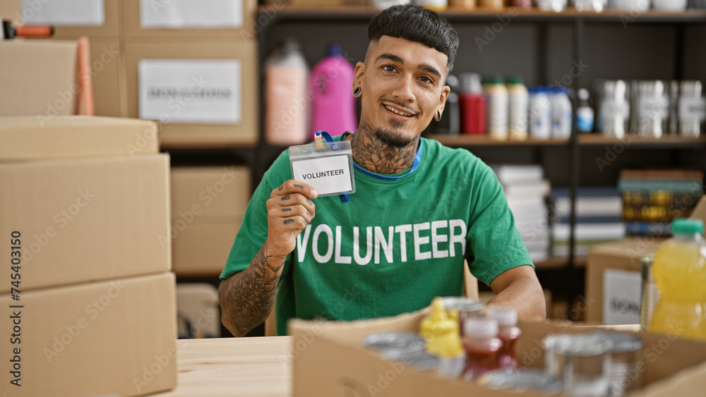 Young, handsome latin man proudly showing off his volunteer id, flashing a confident smile at the heart of a bustling charity center Young, handsome latin man proudly showing off his volunteer id, flashing a confident smile at the heart of a bustling charity center