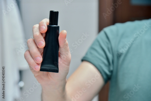 Hand of man holds black tube of cosmetic cream in bathroom