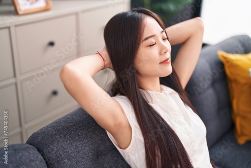 Young chinese woman relaxed with hands on head sitting on sofa at home