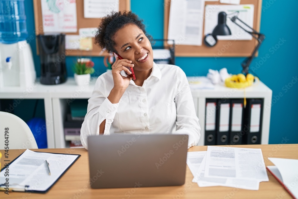 African american woman business worker using laptop talking on smartphone at office African american woman business worker using laptop talking on smartphone at office