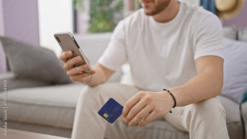 Young hispanic man shopping with smartphone and credit card sitting on sofa at home