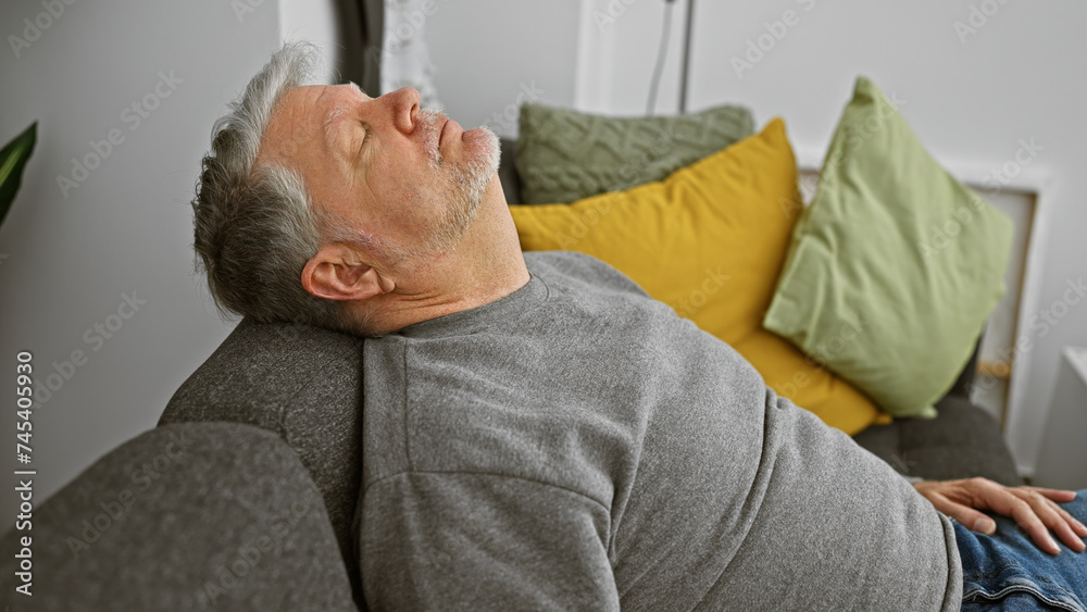 Middle-aged man resting on a couch at home with eyes closed and a serene expression, in a casual setting. Middle-aged man resting on a couch at home with eyes closed and a serene expression, in a casual setting.
