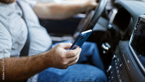 Handsome middle-aged caucasian man sitting in car  texting on smartphone during urban road trip