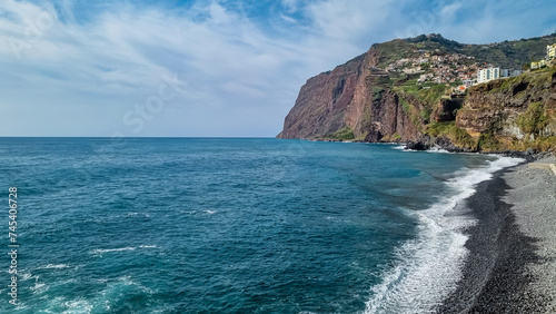 Panoramic view of Praia de Vigario in Camara de Lobos on Madeira island, Portugal, Europe. Black stone beach in Atlantic Ocean. Colourful house on steep hills and cliffs. Paradise travel destination photo