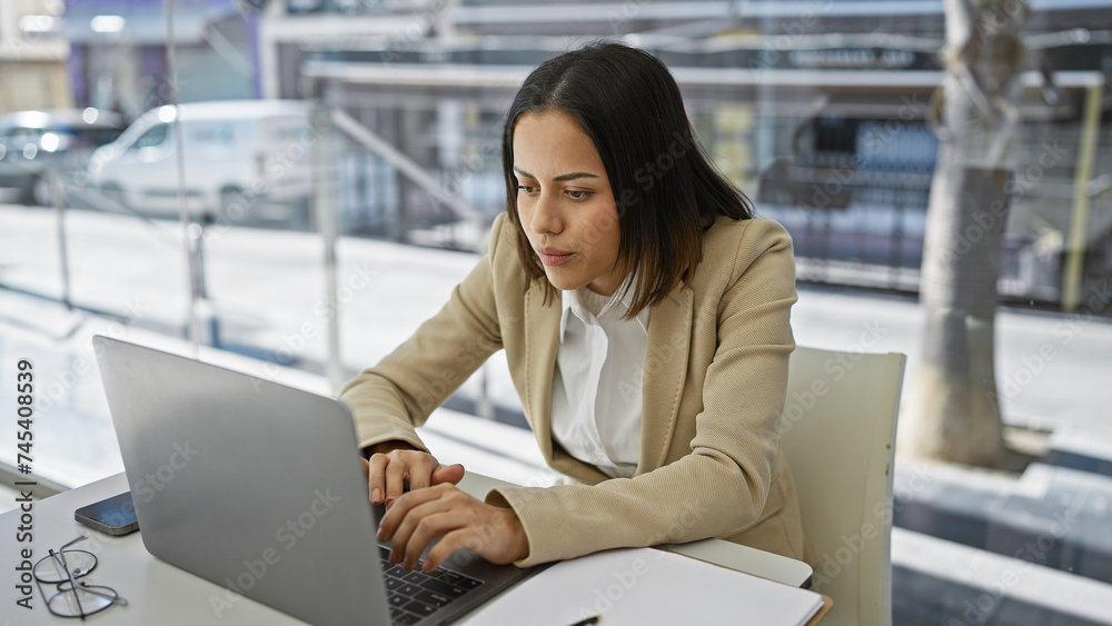 Focused hispanic woman working on her laptop at a modern office desk, exemplifying professionalism and concentration. Focused hispanic woman working on her laptop at a modern office desk, exemplifying professionalism and concentration.