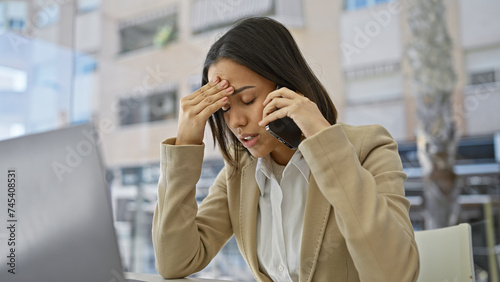 Photos Stressed hispanic businesswoman on phone in office, against a blurred indoor backdrop