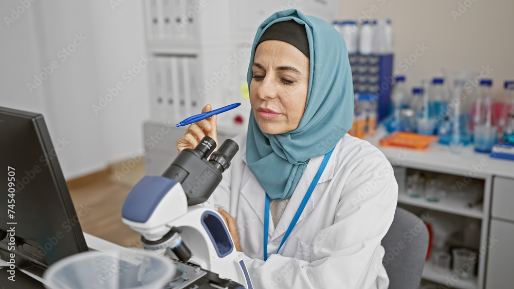 A woman scientist in a hijab examines a slide under the microscope at a laboratory. A woman scientist in a hijab examines a slide under the microscope at a laboratory.