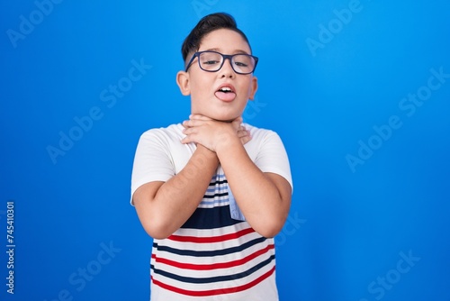 Young hispanic kid standing over blue background shouting and suffocate because painful strangle. health problem. asphyxiate and suicide concept.