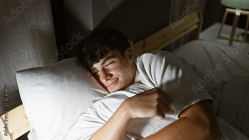 Young hispanic teenager comfortably lying on bed hugging pillow, lost in thoughts in cozy bedroom
