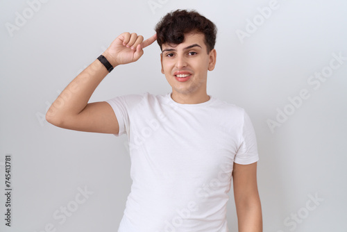 Young non binary man wearing casual white t shirt smiling pointing to head with one finger, great idea or thought, good memory