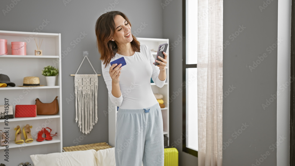 Smiling woman holding credit card and smartphone in a modern bedroom, shopping online. Smiling woman holding credit card and smartphone in a modern bedroom, shopping online.