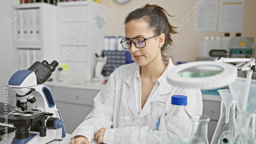 A young hispanic woman scientist analyzes samples in a laboratory setting, surrounded by equipment and glassware.
