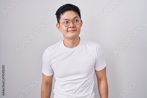 Young asian man standing over white background smiling looking to the side and staring away thinking.