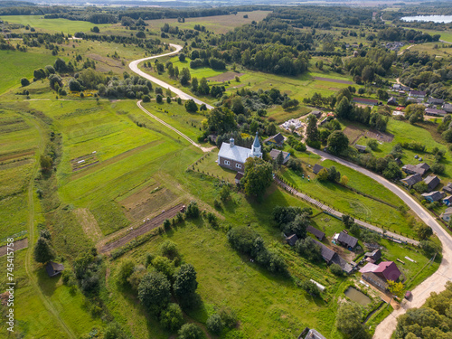 Top view of a small village in the middle of a green field and forest. An old church on a hill in the center of the city. Aerial view of the farm field and the natural landscape. © Pokoman