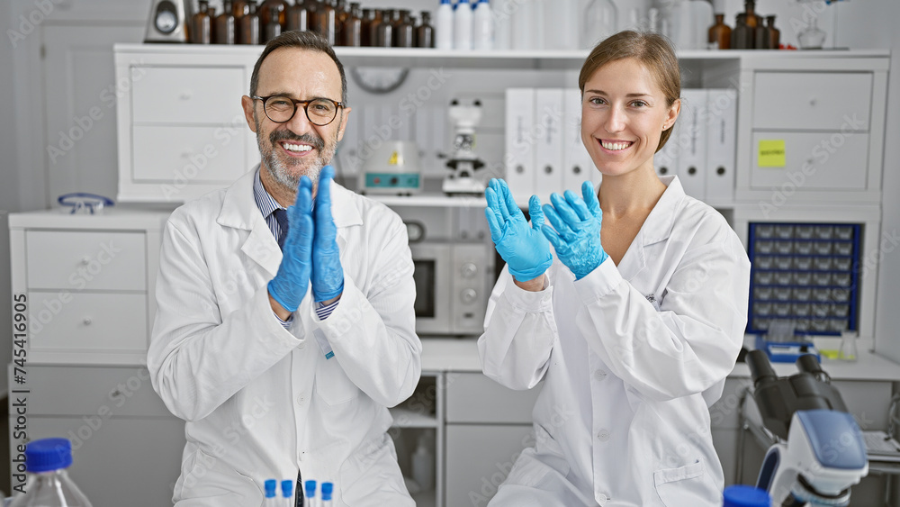 Two smiling scientists clapping hands in applause, celebrating major research breakthrough in their lab Two smiling scientists clapping hands in applause, celebrating major research breakthrough in their lab