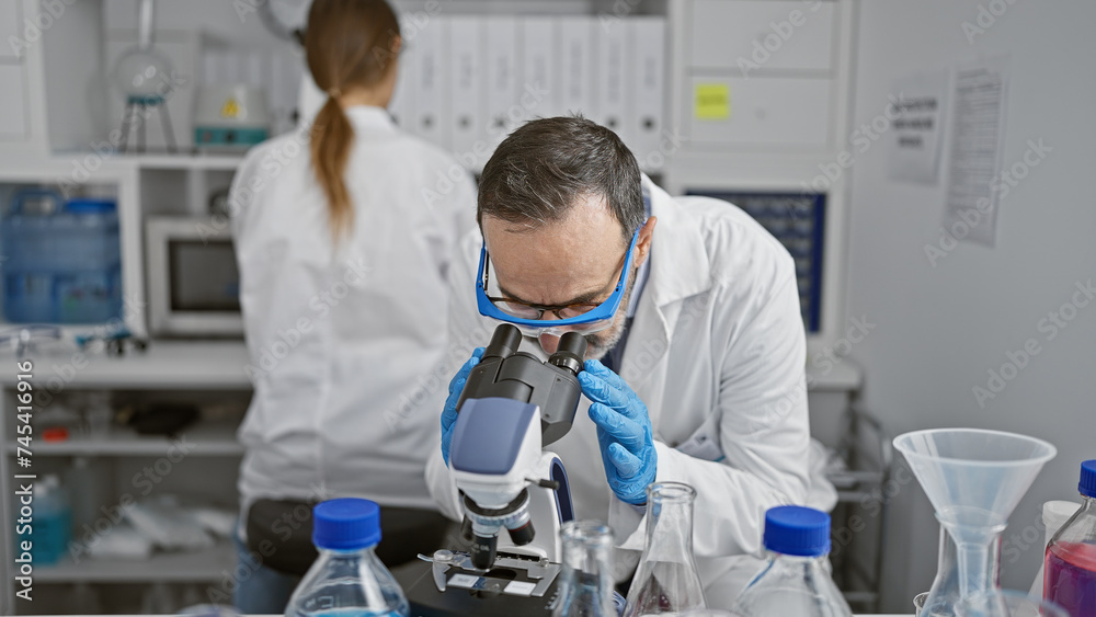 Two dedicated scientists, team mates working together indoors in a lab, busy with serious research using a microscope, discovering new analysis in medical science. Two dedicated scientists, team mates working together indoors in a lab, busy with serious research using a microscope, discovering new analysis in medical science.