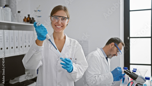Two joyful lab mates, woman and man, pouring liquid into a sample pipette together, navigating the path of medical science, gloves on for safety in a bustling laboratory interior. photo