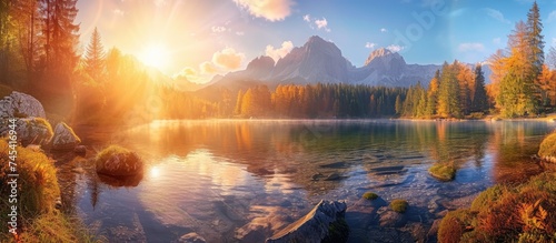 The painting depicts a mountain lake at sunset, showcasing the Mongart mountain and Fusine Lake under the warm glow of the setting sun. The scene captures the beauty and tranquility of the fall