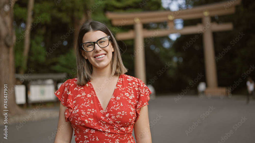 Cheerful, beautiful hispanic woman with glasses poses confidently, smiling at tokyo's meiji shrine, her joy unequivocally radiating through her astonishing smile