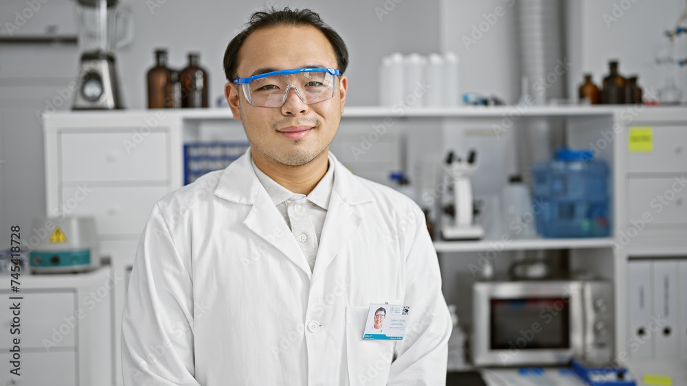 Confident young chinese scientist enjoys his work, smiling happily while standing in the bustling lab, amidst the thrill of medical research and technology.